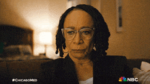 a woman wearing glasses sits on a couch with a nbc logo on the bottom