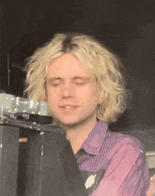 a man with blonde curly hair is wearing a purple and white striped shirt