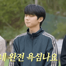 a young man wearing a blue adidas jacket stands with his eyes closed in front of a sign in korean