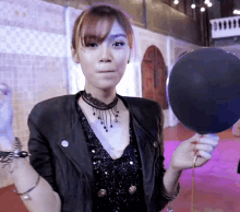 a woman in a black jacket is holding a black balloon in her hand
