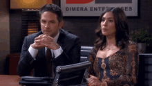 a man and a woman sit in front of a dimera enterprise sign