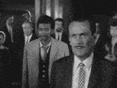 a man in a suit and tie stands in front of a crowd of men