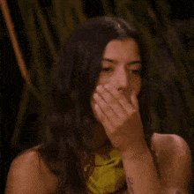 a woman is covering her mouth with her hand while wearing a yellow top .