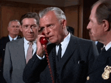 a man in a suit and tie talks on a red telephone
