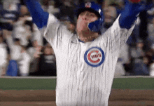 a man wearing a chicago cubs jersey is raising his arms in the air