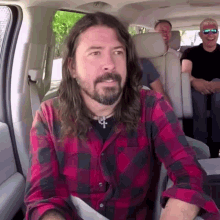 a man with long hair and a beard is sitting in the back seat of a vehicle