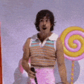 a man in a striped shirt and pink shorts is holding a microphone and a lollipop .