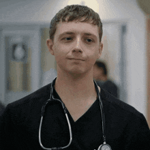 a man wearing a black scrub top and a stethoscope around his neck looks at the camera