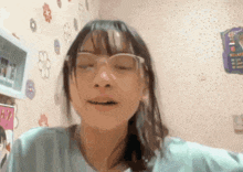 a girl wearing glasses is making a funny face in front of a wall with flowers on it .