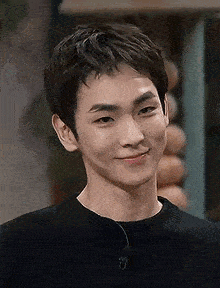 a young man wearing a black sweater is smiling and looking at the camera