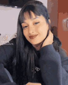 a woman with long black hair and bangs is wearing a black hoodie and looking at the camera .