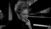 a black and white photo of a woman smoking a cigarette while sitting in front of a piano .