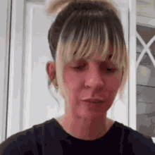 a woman with blonde hair and bangs is wearing a black t-shirt and a bun .