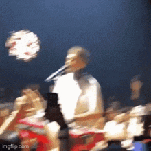 a blurry picture of a man singing into a microphone in front of a crowd of people .