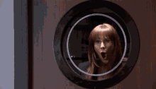 a woman with red hair looks through a round window