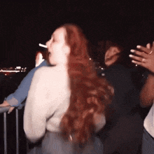 a woman with long red hair is dancing in a crowd at night
