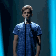 a young man singing into a microphone with a blue shirt on