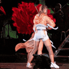 a couple of women are dancing on a stage with a red flower in the background
