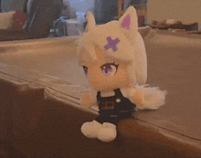 a white stuffed animal with a purple cross on its head sits on a table