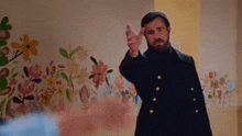a man with a beard is pointing at something in front of a floral wall