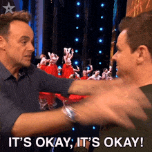 two men are hugging each other with the words it 's okay it 's okay behind them
