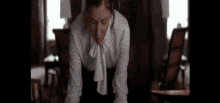 a woman in a white polka dot shirt is kneeling down in a dark room