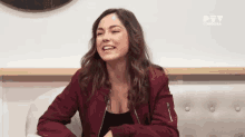 a woman in a red jacket is sitting on a white couch and smiling .