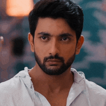 a man with a beard wearing a white shirt looks at the camera