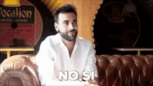 a man in a white shirt is sitting on a brown leather couch and says no si