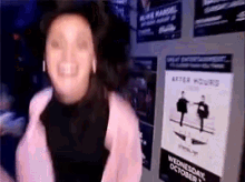 a woman in a pink coat is dancing in front of a wall with posters on it .