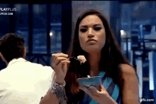 a woman is eating food from a bowl with a fork while a man looks on .