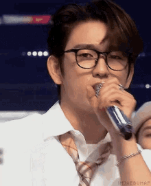 a man wearing glasses and a tie is holding a microphone in his mouth .