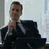 a man in a suit and tie is sitting at a desk with a laptop