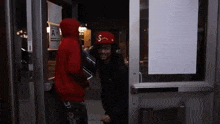 a man in a red hoodie and a red hat is standing in a doorway .