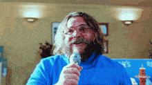 a man with glasses and a beard is singing into a microphone in front of a sign that says ' s'
