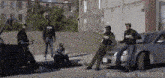 a group of men are standing around a car and a truck .