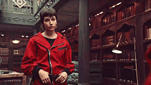 a man in a red jacket is standing in a room looking up .