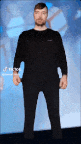 a man in a black shirt and black pants is standing in front of a blue background with tiktok written on the bottom right corner
