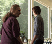 a woman in a purple shirt stands next to a man in a blue shirt on a porch