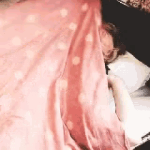 a person is laying on a bed with a pink blanket and a pillow .