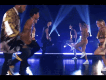 a group of people are dancing on a stage in front of a blue light