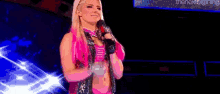 a woman in a pink outfit is holding a microphone and smiling on a stage .