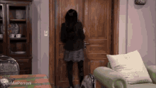 a woman in a black skirt is standing in front of a wooden door with the name sue mai perroni on the bottom right