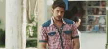 a man in a plaid shirt and denim shorts is standing in front of a store .