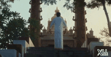 a man in a white shirt is walking up a set of stairs in front of a building with the letters xhk visible
