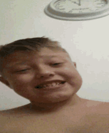 a young boy is smiling in front of a wall clock that shows the time as 7:15