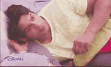 a man in a yellow shirt is laying on a bed with the words " shubhs " on the bottom right