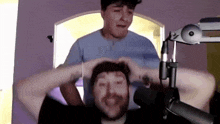 two men are standing next to each other in front of a microphone and one of them is holding the other 's head .