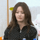 a woman wearing a black polka dot jacket is sitting in front of a hello kitty doll .