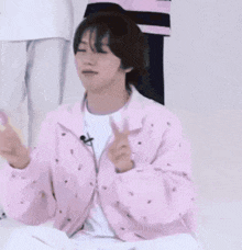 a young man in a pink jacket is giving a peace sign while sitting on the floor .